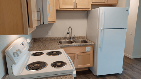A white stove with four burners is in a kitchen with a white refrigerator.