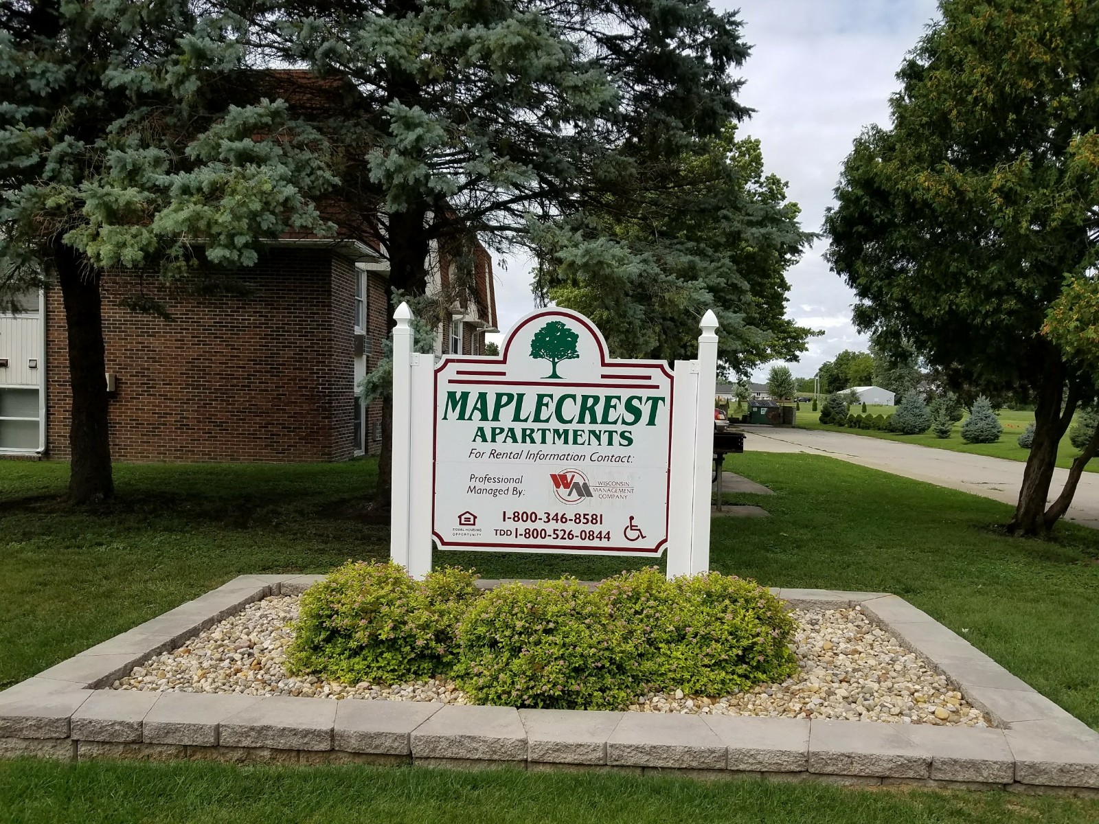 the sign for maple crest apartments in front of a lawn and trees