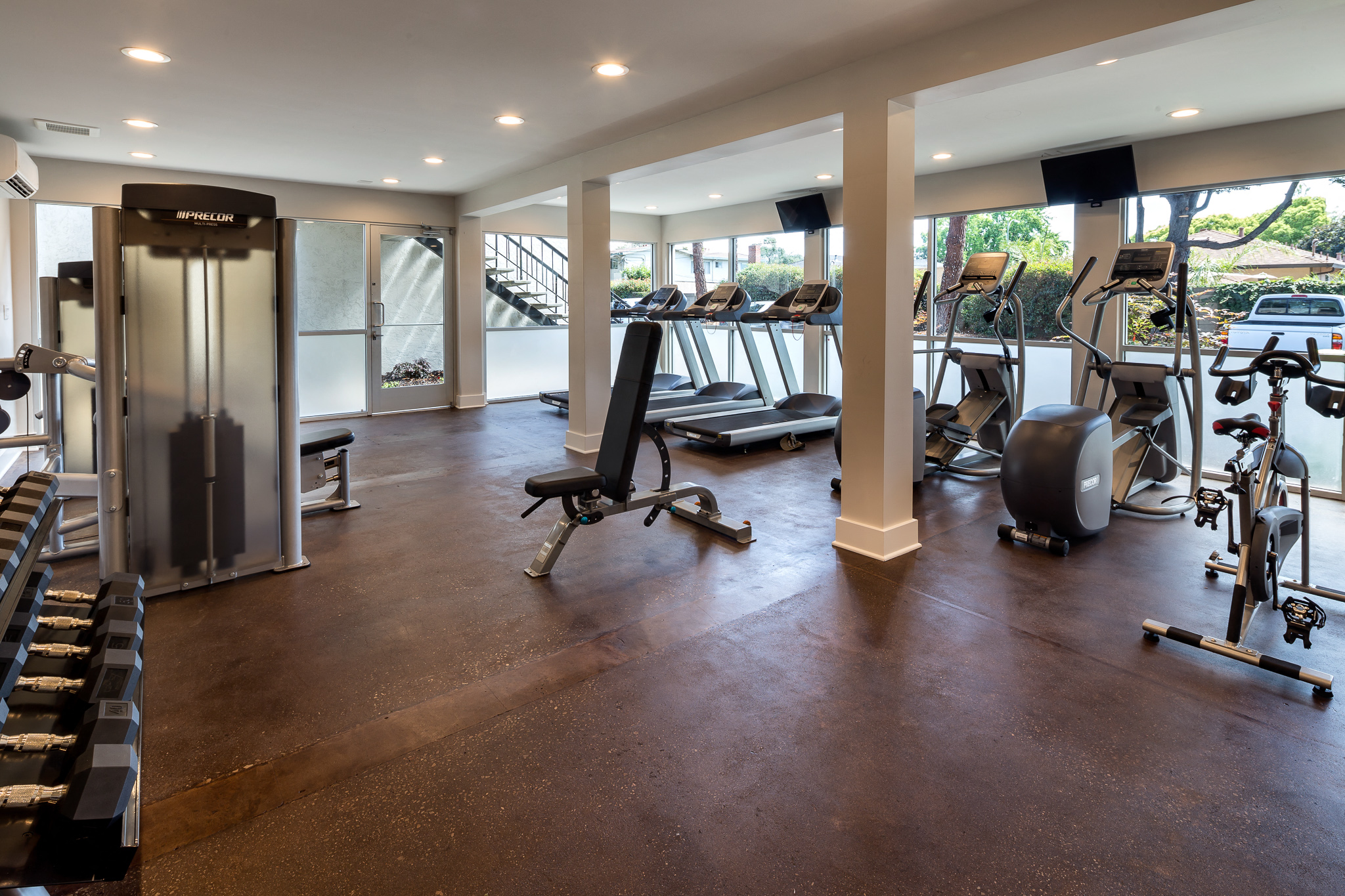 a gym with weights and cardio equipment on the floor and a staircase