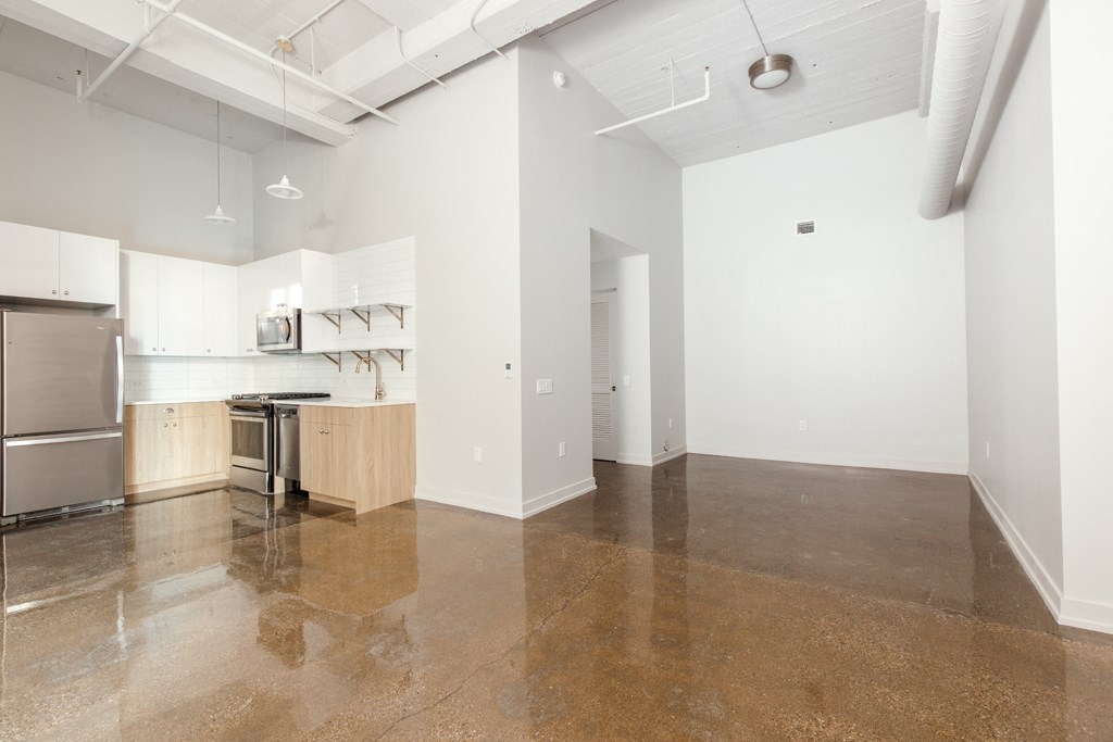an empty kitchen and living room with white walls and concrete floors