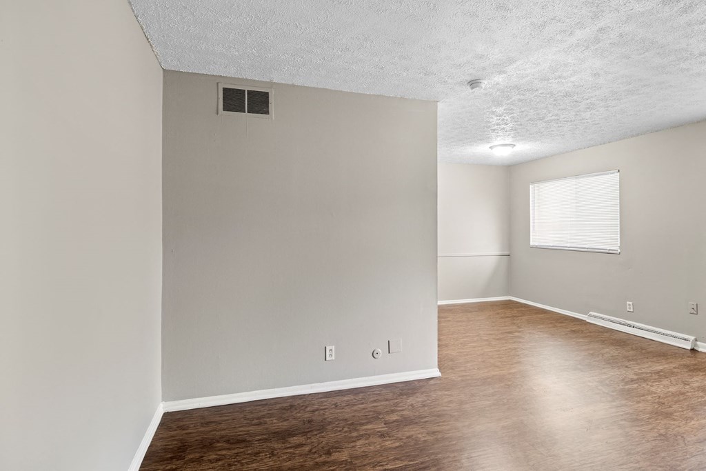 an empty living room and dining room with wood flooring and a window