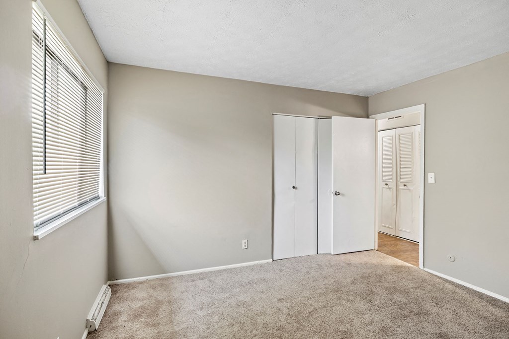 an empty bedroom with a window and a closet