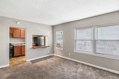 an empty living room with a kitchen in the background