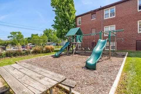 a playground with slides and a picnic table in front of a brick building