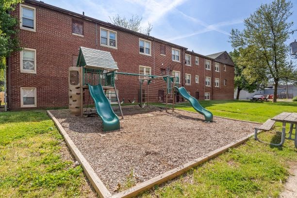 a playground with three slides in front of a brick building