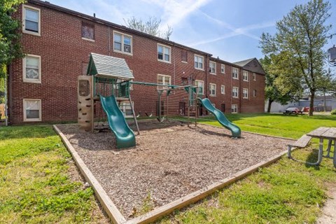 a playground with three slides in front of a brick building