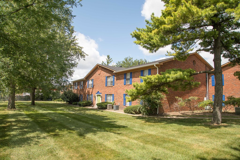the front of a brick apartment building with grass and trees