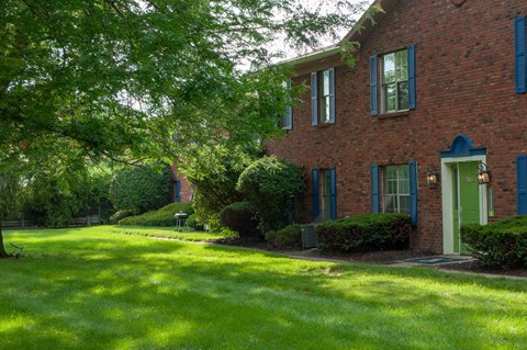 the front of a brick house with green grass and trees