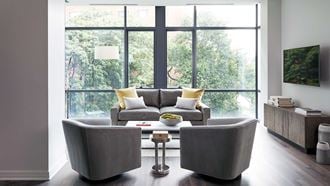 A living room set with two chairs facing a couch sits before floor-to-ceiling windows.