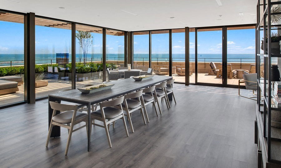 A long dinging room table sits in a open room with floor-to-celing windows. The sky terrace is seen outside and Lake Michigan beyond on a sunny day.