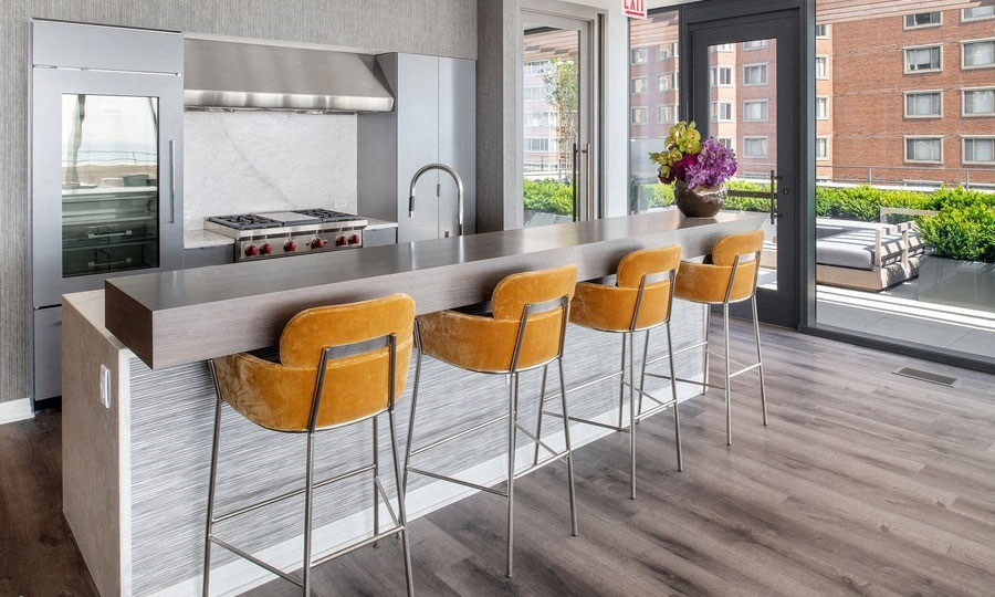 Orange bar chairs site before the bar and commercial kitchen in the rooftop club. A large cooktop is seen behind the bar.