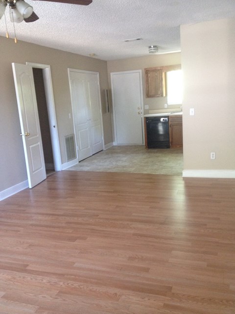 an empty living room with wooden floors and a kitchen