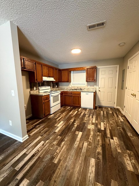 A kitchen with white appliances and wooden floors.