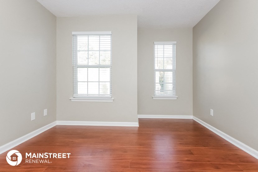the interior of an empty room with wood floors and two windows