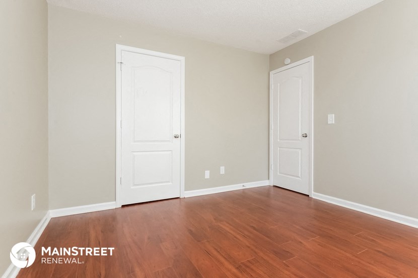 the living room of an apartment with wood flooring and two doors