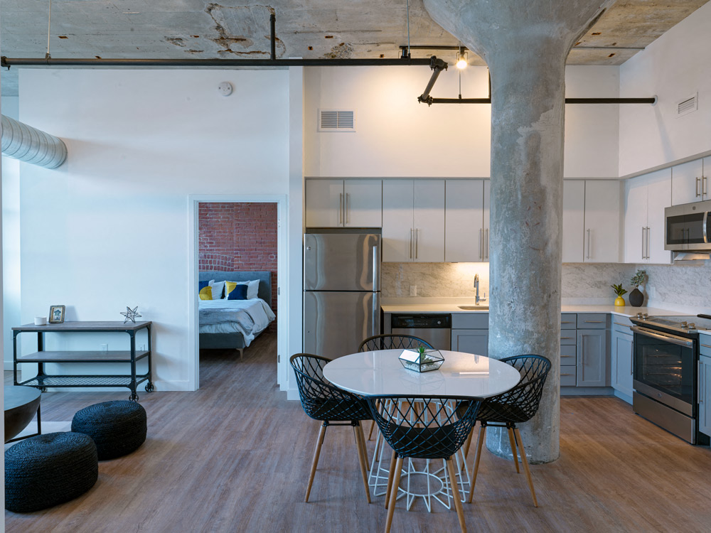 A kitchen with a table and chairs in the foreground and a bedroom in the background.