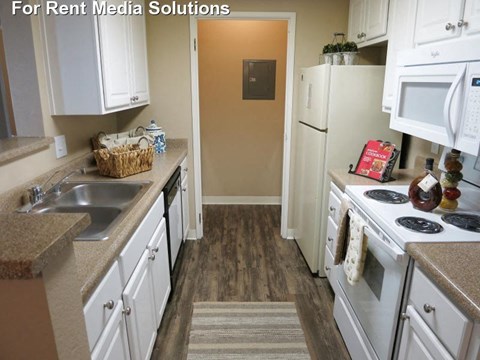 A kitchen with white cabinets and appliances, a sink, and a door in the background.