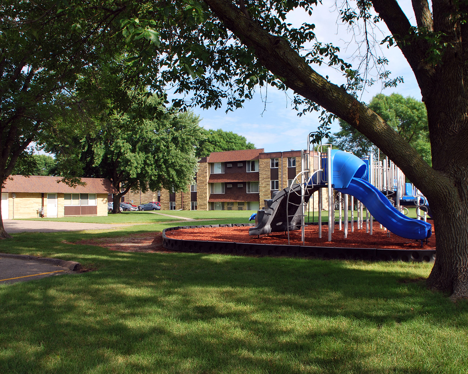 a playground with a blue slide in front of an apartment building