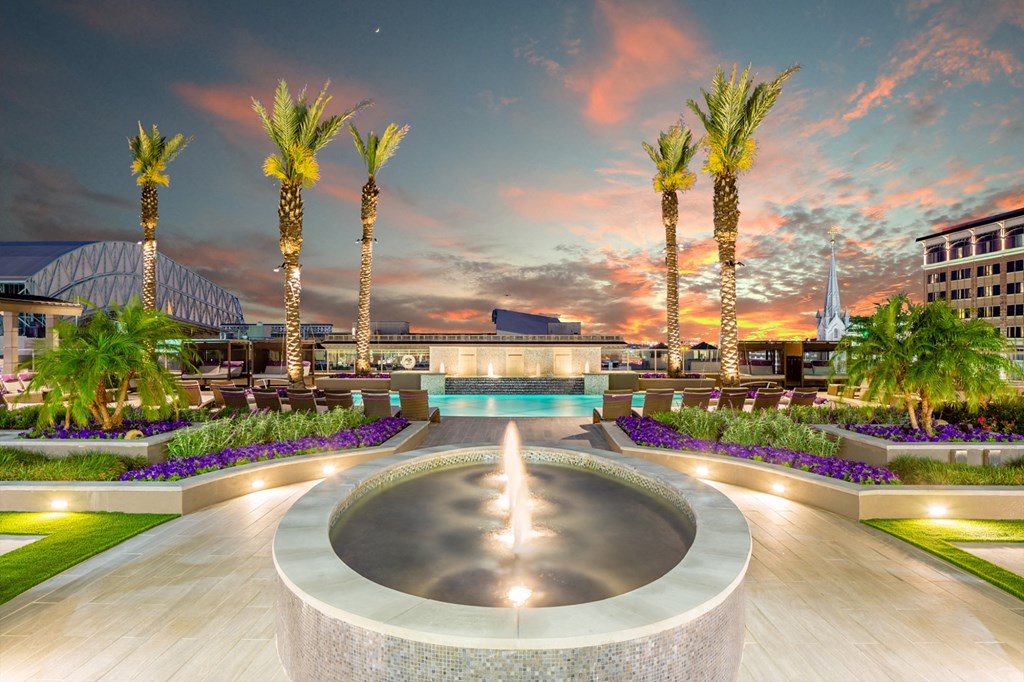 a fountain at night with palm trees and a sunset in the background