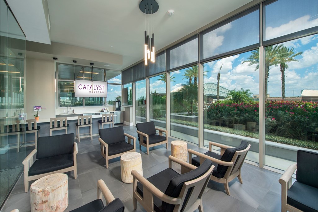 a lobby of a hotel with chairs and a bar and large windows