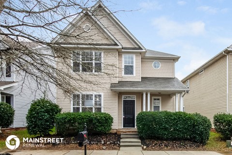 a tan house with a black door and manicured bushes