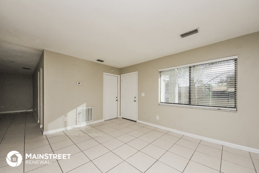an empty living room with a window and a white tiled floor