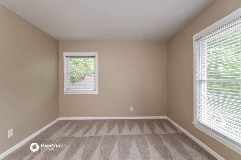 an empty bedroom with two windows and a carpeted floor