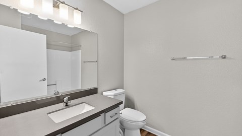 A bathroom with a toilet, sink, mirror, and light fixture.
