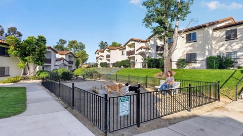 A woman is sitting on a bench next to a black fence with a dog on it.