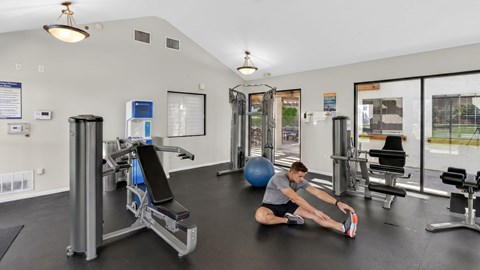 A man is stretching in a gym with a blue exercise ball.