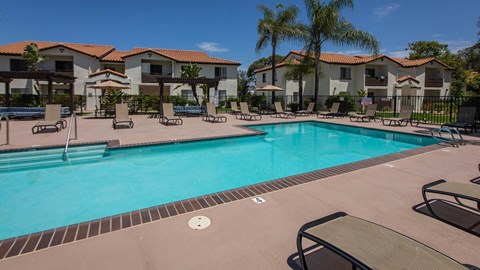 A swimming pool surrounded by lounge chairs and palm trees.