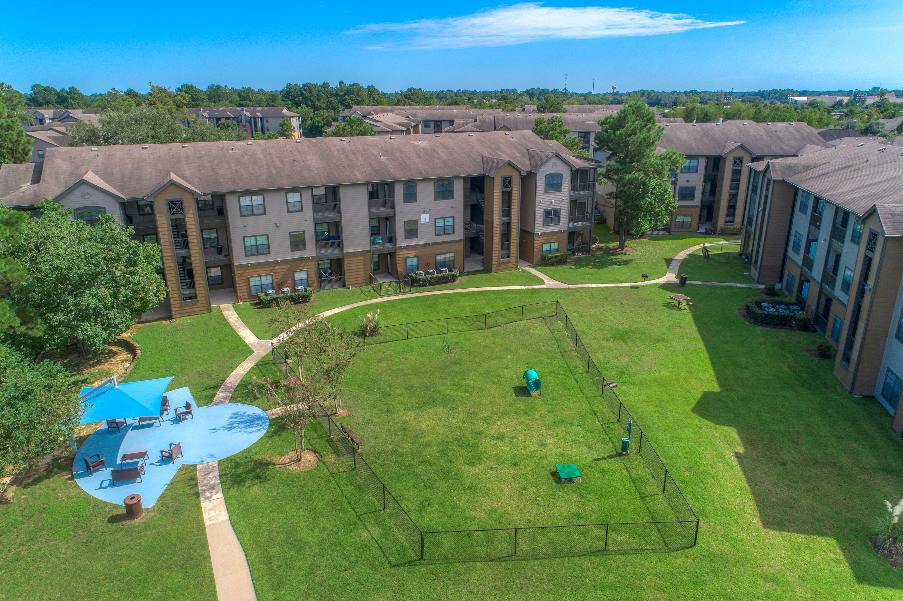 Dog-Friendly Apartments in Spring, TX - Overhead View of Fenced off Dog Park with Seperate Covered Seating Area Surrounded by Lush Greenery.