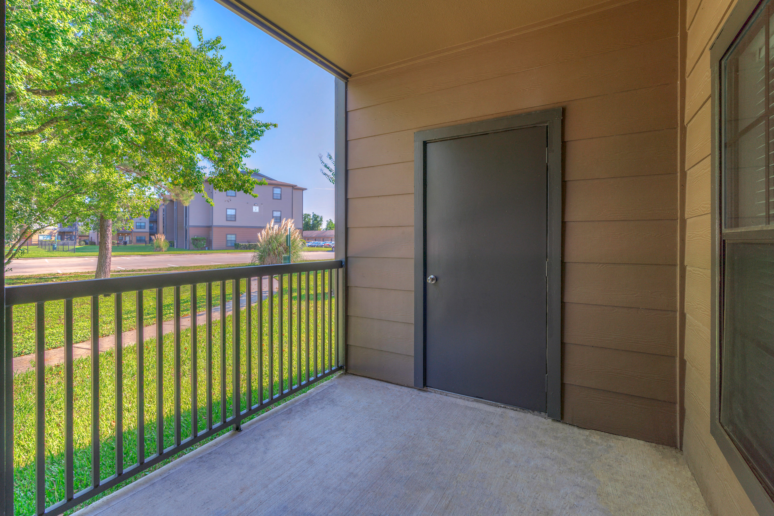 Pet-Friendly Apartments in Spring, TX - Spacious Patio with Metal Railing, a Storage Room and a View of Grass and Trees.