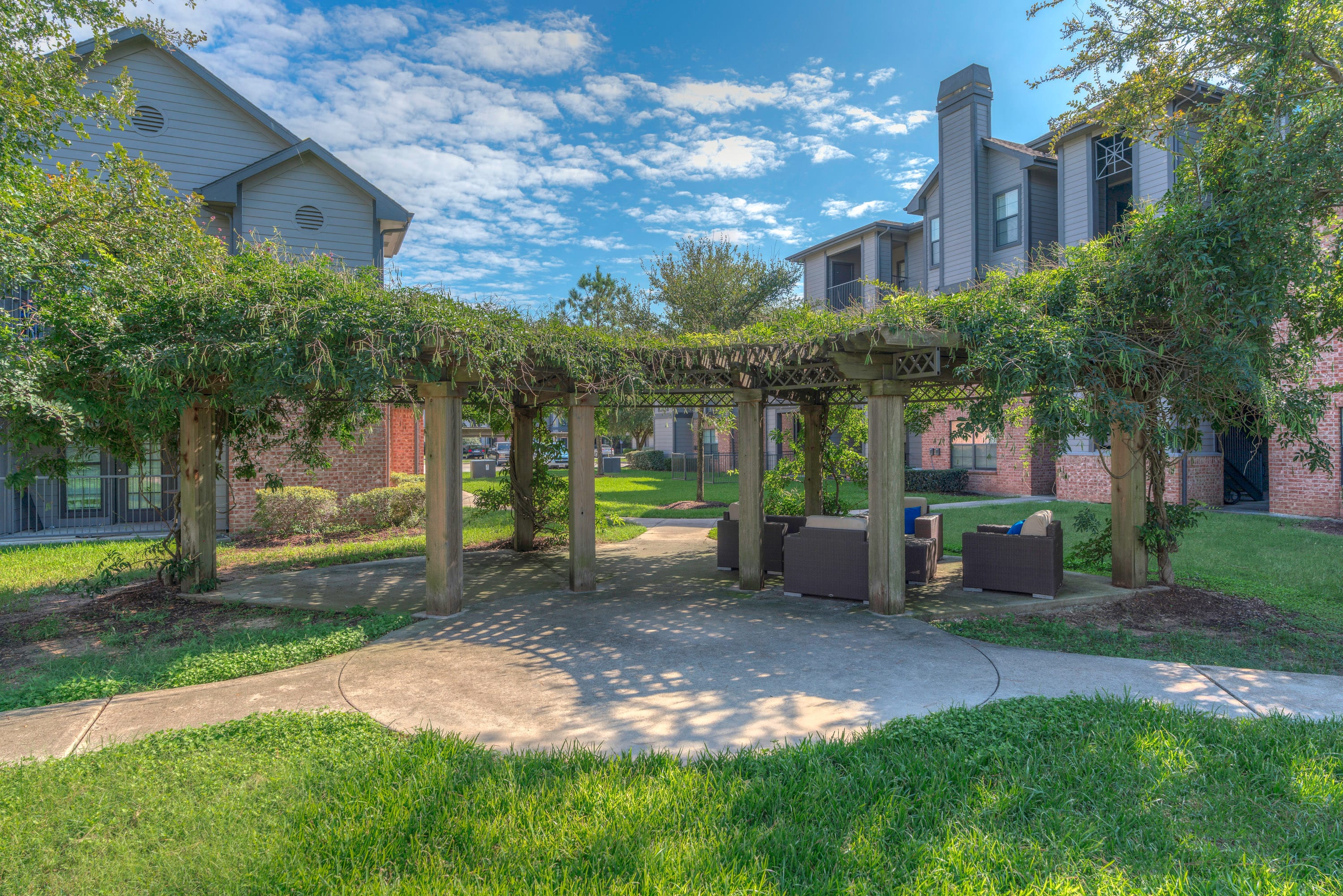 a pergola with benches and trees in front of an apartment building