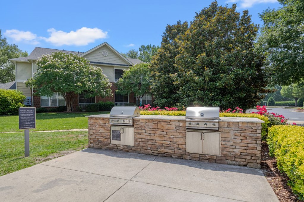 a stone retaining wall with two barbecue grills in front of a house