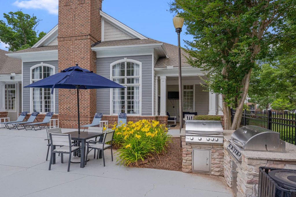 a patio with an umbrella and tables with chairs and a grill