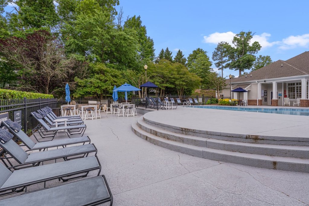 a pool with lounge chairs and umbrellas next to a house