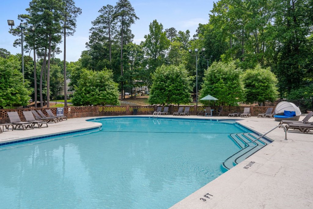 a swimming pool with chairs and trees in the background