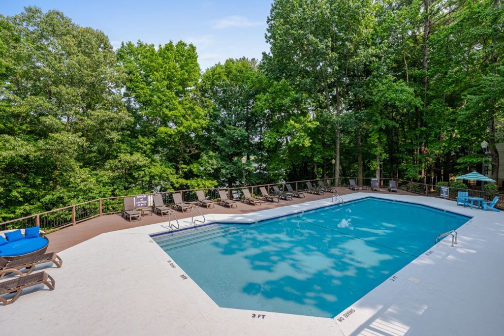 a swimming pool with lounge chairs and trees in the background