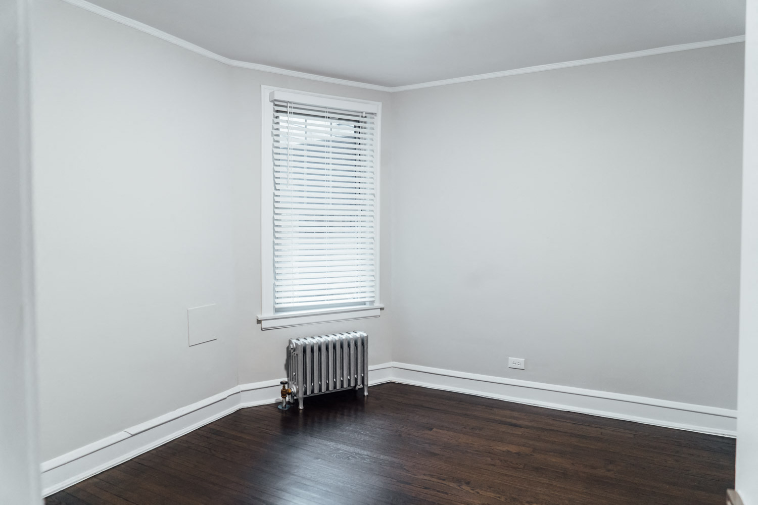 an empty room with white walls and wood floors and a radiator