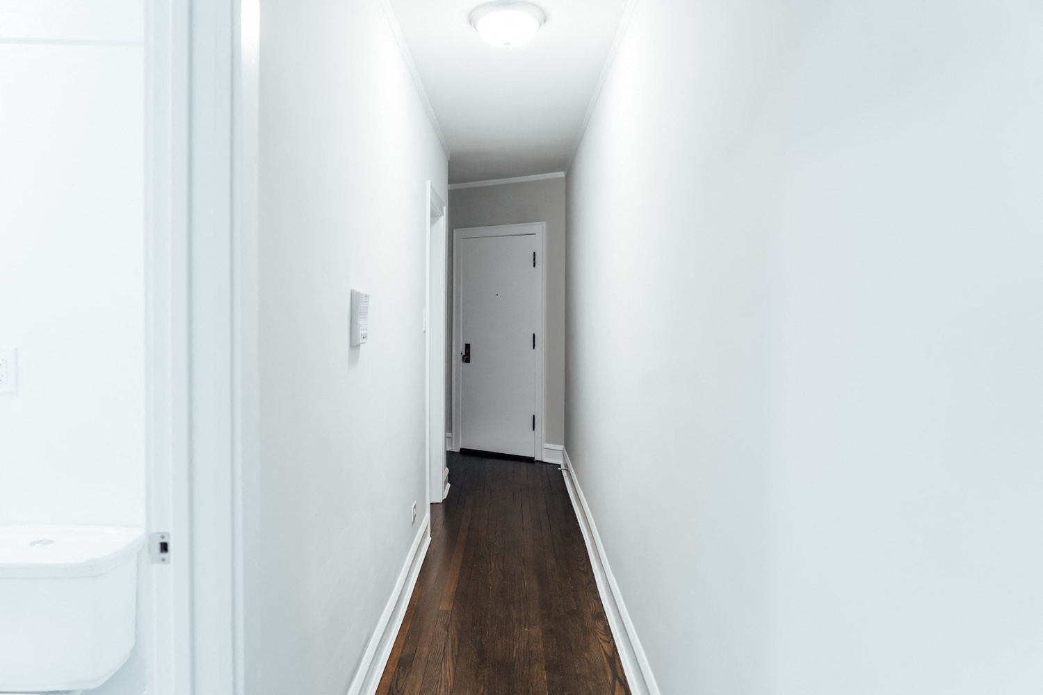 a hallway with white walls and wood floors and a white door