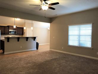 an empty living room with a kitchen and a ceiling fan