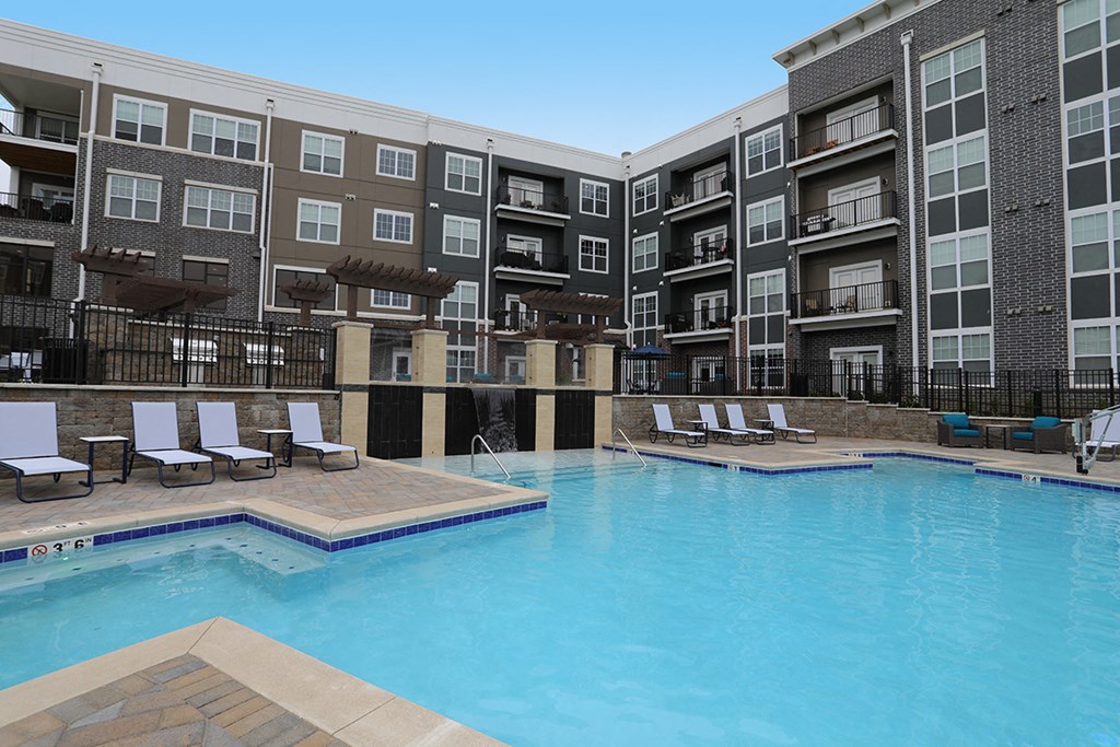 a swimming pool with lounge chairs in front of an apartment building