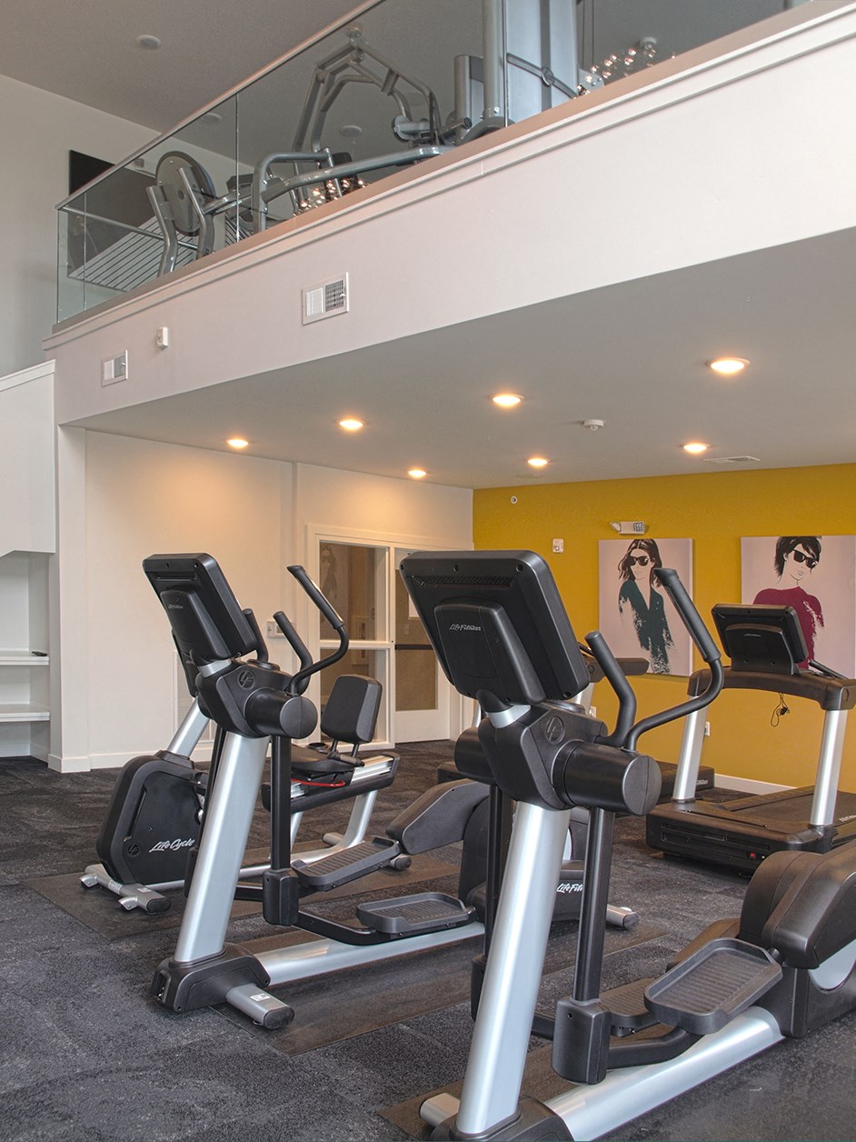 a gym with cardio machines and a staircase in the ceiling