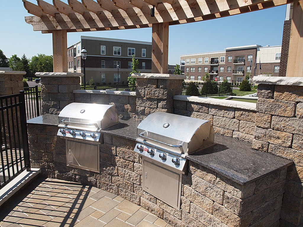 two stainless steel grills on a stone wall with a pergola