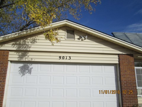 A white garage door with the number 9013 on the wall above it.
