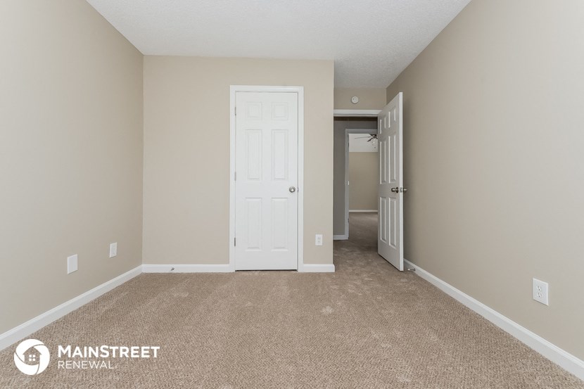a spacious bedroom with carpeted flooring and a door to the hallway