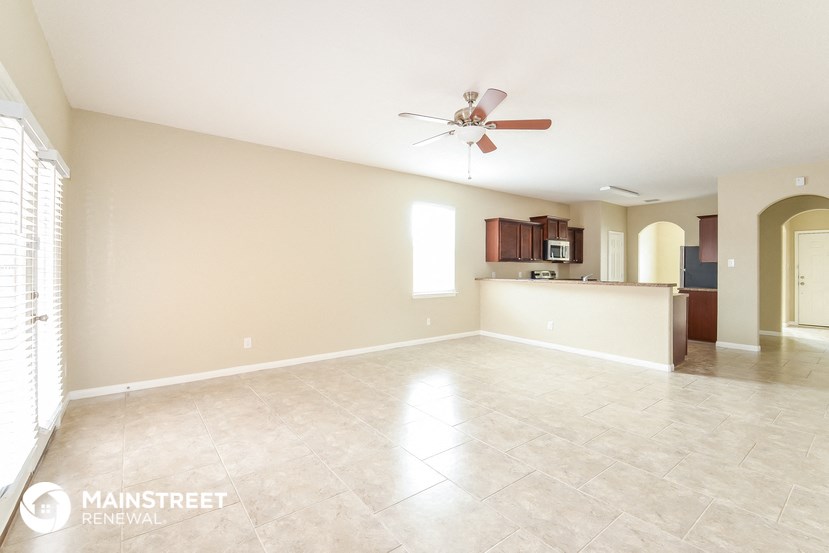 an empty living room with a kitchen and a ceiling fan