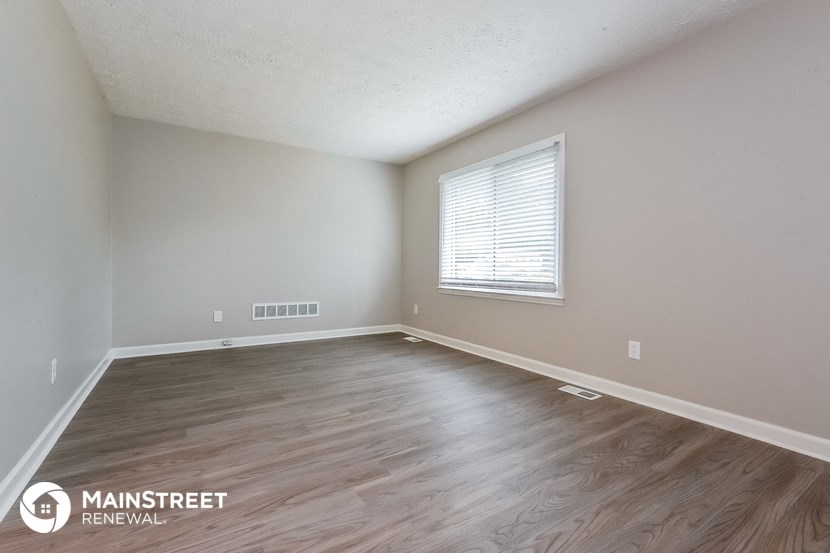 the spacious living room with wood flooring and a window