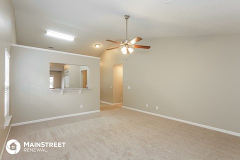 a spacious living room with carpet and a ceiling fan